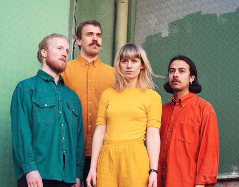 Fyra bandmedlemmar i färgglada käder framför en grön vägg